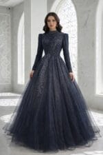 Şahbanu lacivert tesettür helen nişan kına abiye elbise - VznModa Woman in a navy blue, sparkly ball gown with long sleeves and a high neckline, standing in a marble hallway.