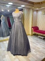 Evening gown on a dress form: silver lace bodice with a full glittery gray skirt in a gold-trimmed boutique window.
