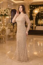 Elegant woman in a sparkling beige evening gown poses in a luxurious banquet hall with chandeliers and white floral decorations.