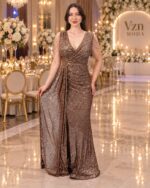 Woman in a glittering bronze evening gown posing in an upscale gala hall with floral arrangements and chandeliers